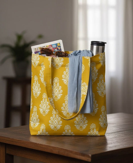 Yellow tote bag with floral pattern on a wooden table, containing a book, a shirt, and a cup.